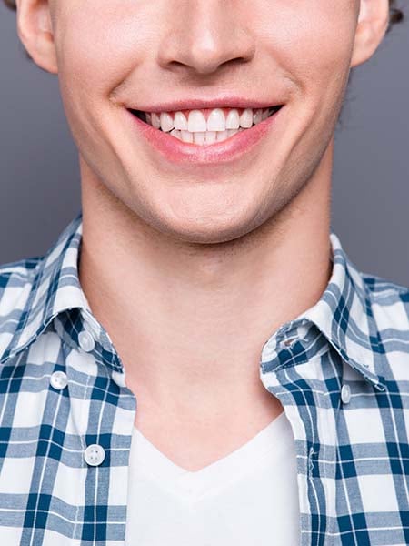types-of-veneers-stylish-guy-blue-checkered-shirt-posing-against-grey-wall-smile-dental-care-oral-health